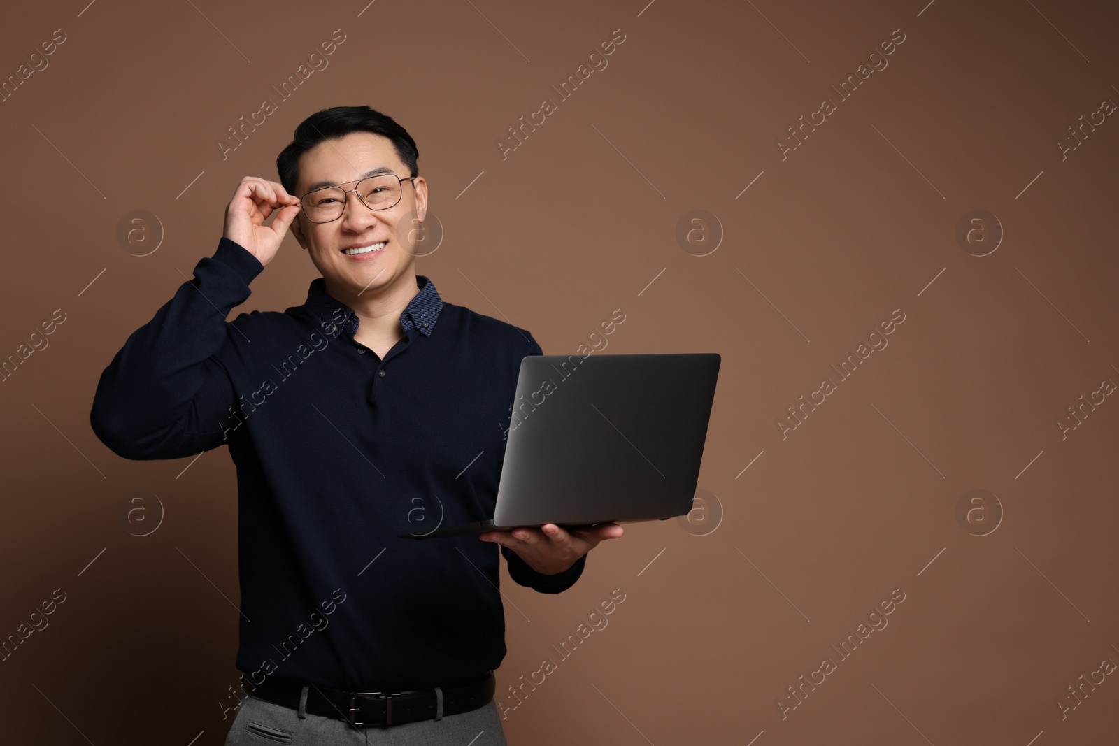 Photo of Portrait of happy man with laptop on brown background. Space for text