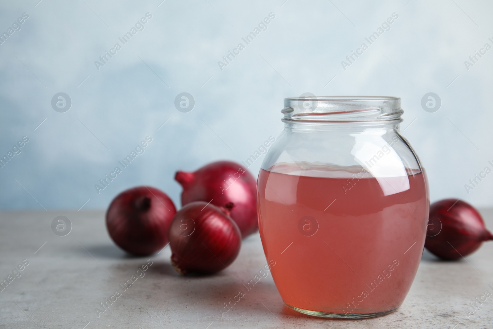 Photo of Glass jar of onion syrup and fresh vegetable on table. Space for text