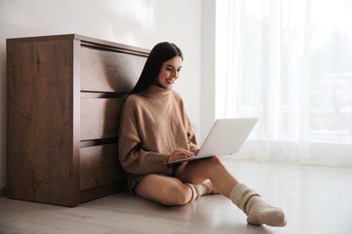 Woman with laptop sitting on warm floor at home. Heating system