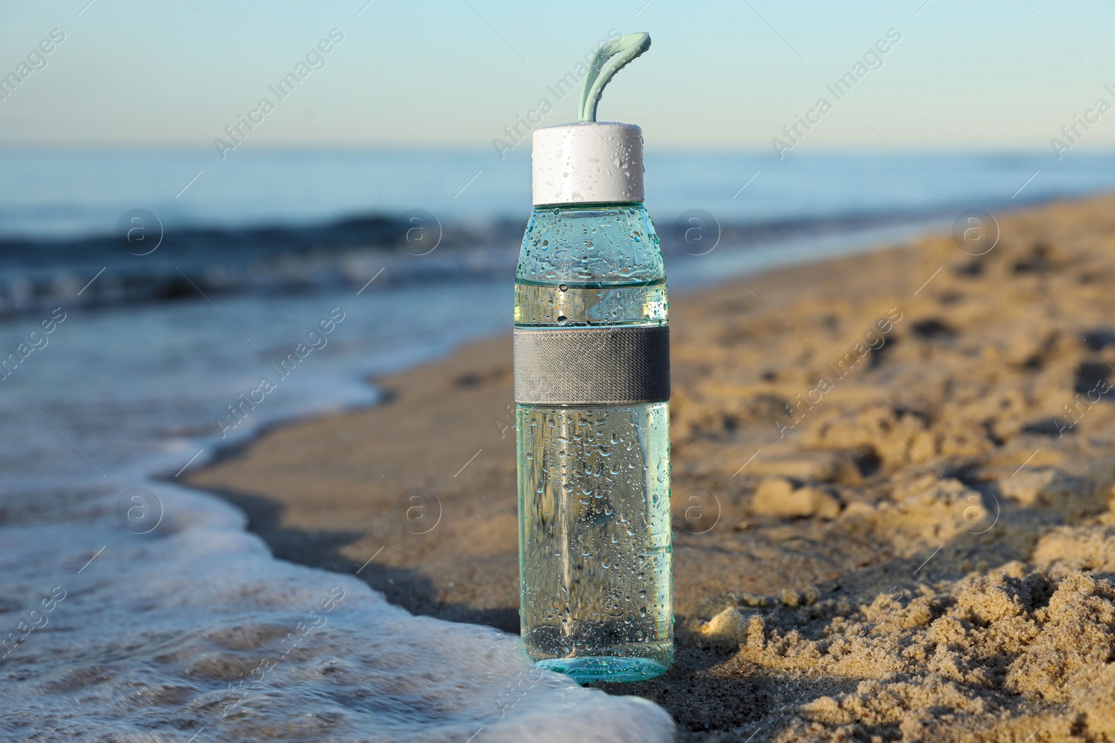 Photo of Glass bottle with water on wet sand near sea