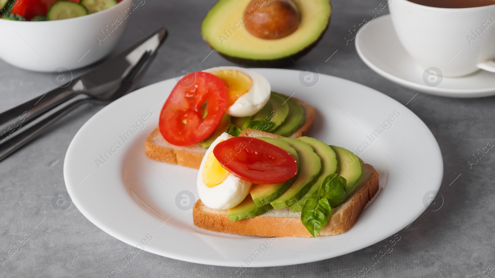 Photo of Tasty sandwiches with boiled egg, avocado and tomato served on grey table