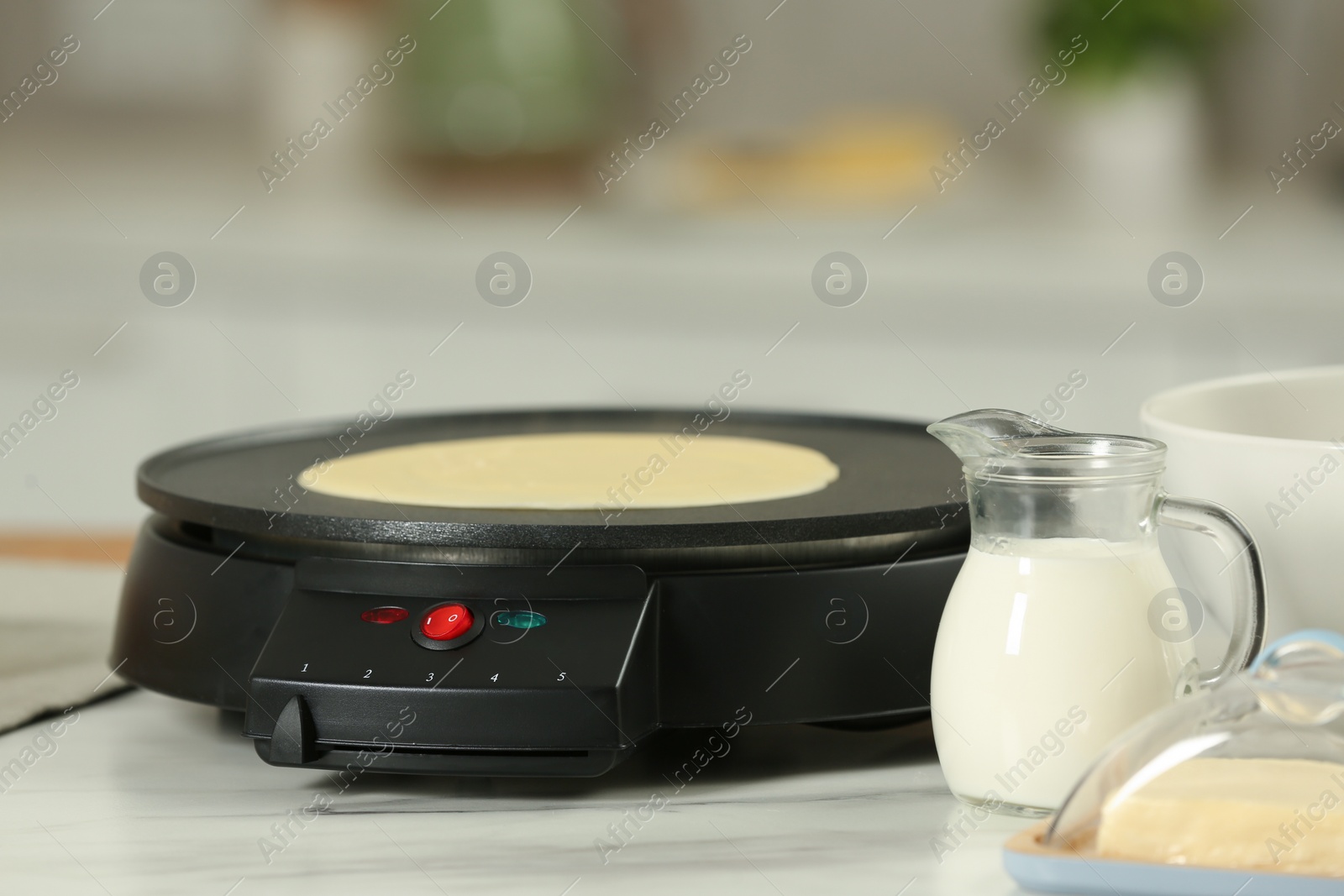 Photo of Electric maker with crepe and ingredients on white marble table in kitchen