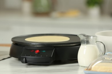 Electric maker with crepe and ingredients on white marble table in kitchen