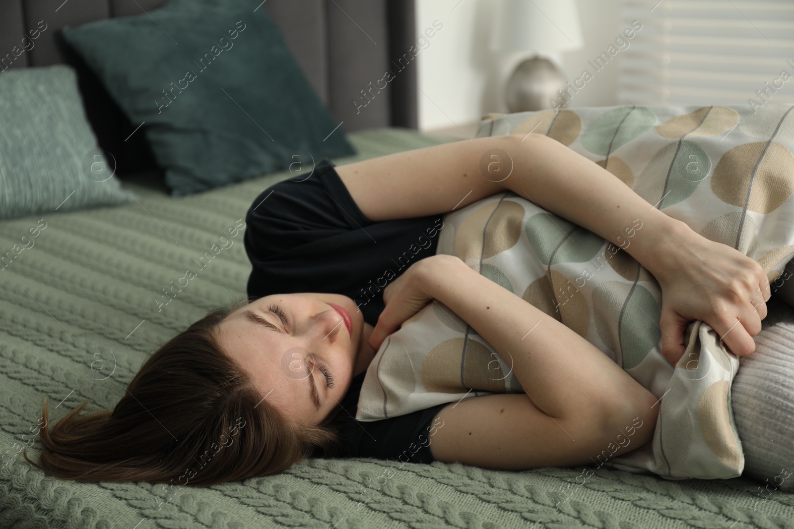 Photo of Sad young woman lying on bed at home