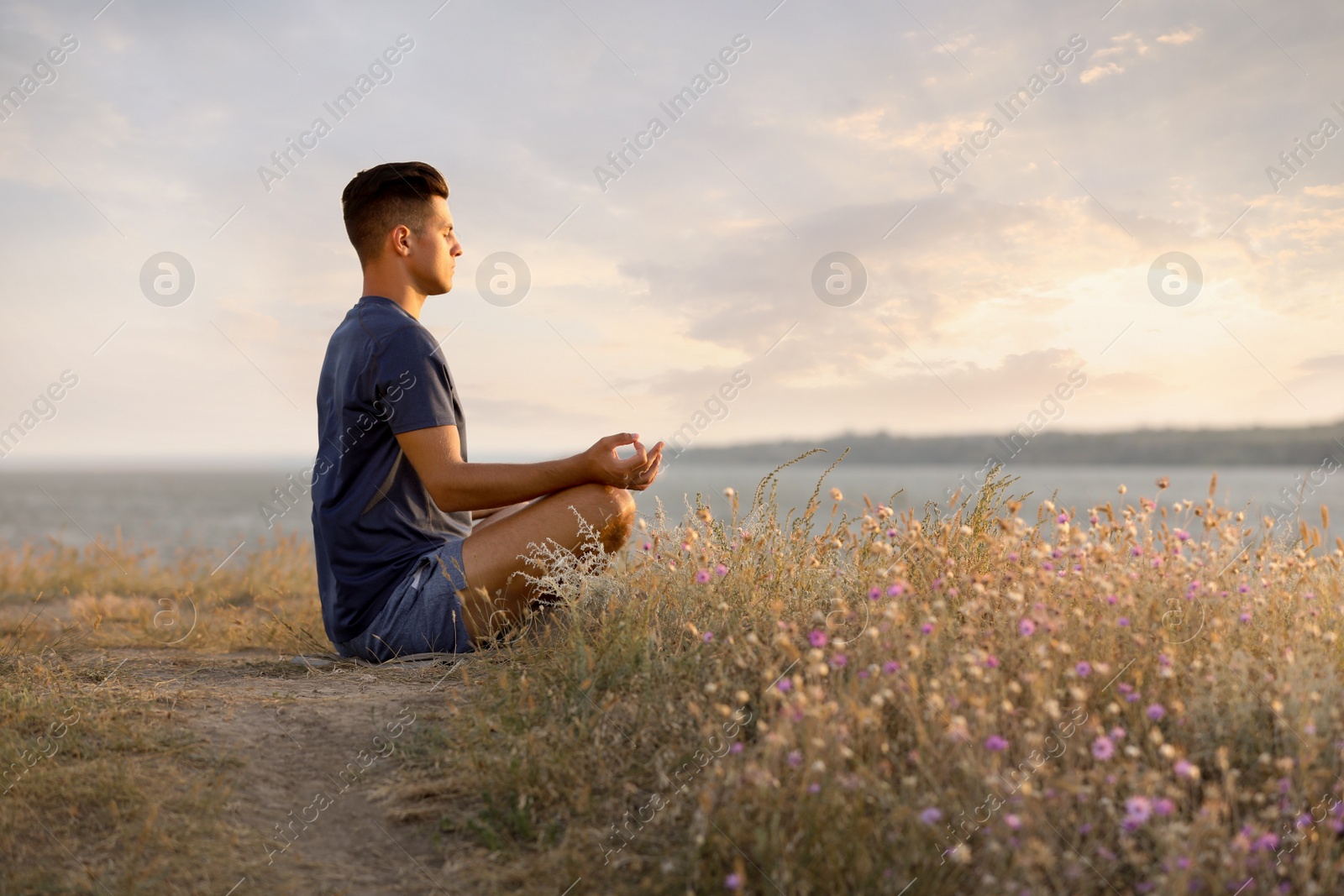 Photo of Man meditating near river on sunny day, space for text