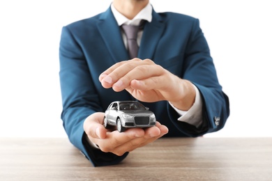 Insurance agent holding toy car in hands over table against white background