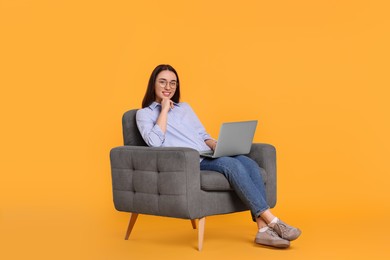 Photo of Smiling young woman with laptop sitting in armchair on yellow background