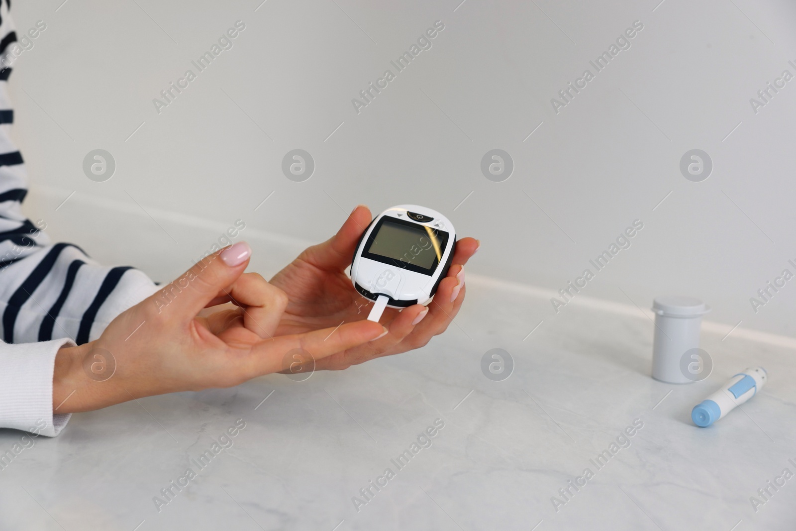 Photo of Diabetes. Woman checking blood sugar level with glucometer at light table, closeup