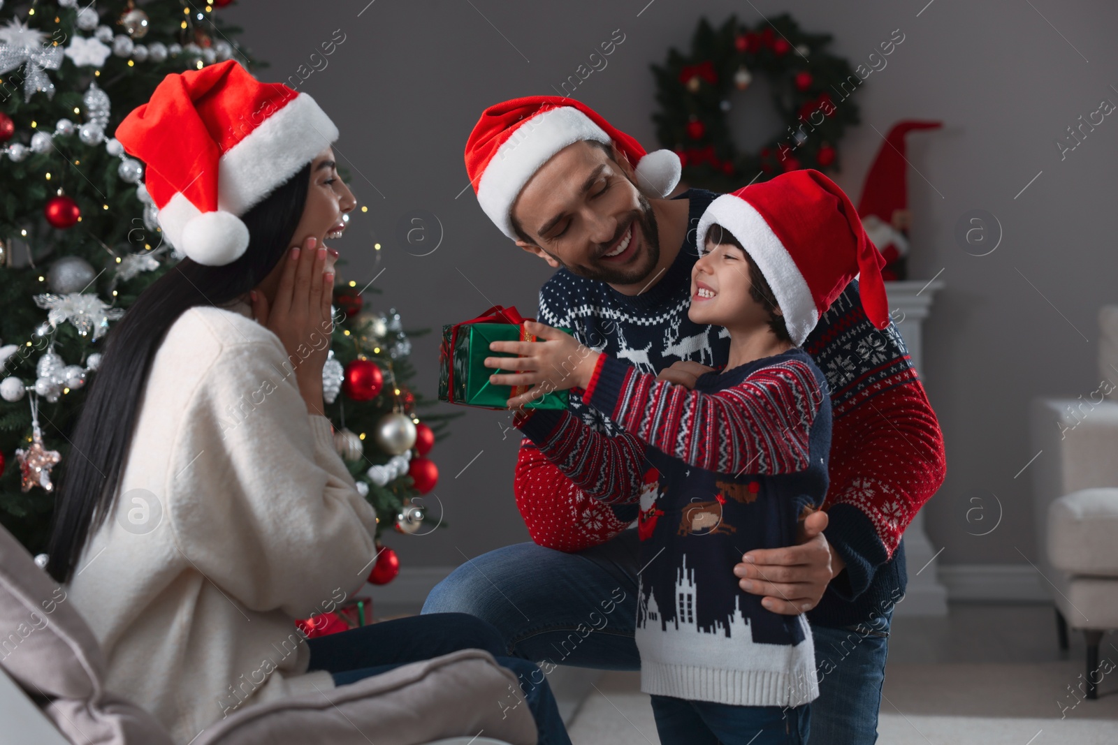 Photo of Father with his cute son presenting gift to mother at home. Christmas celebration