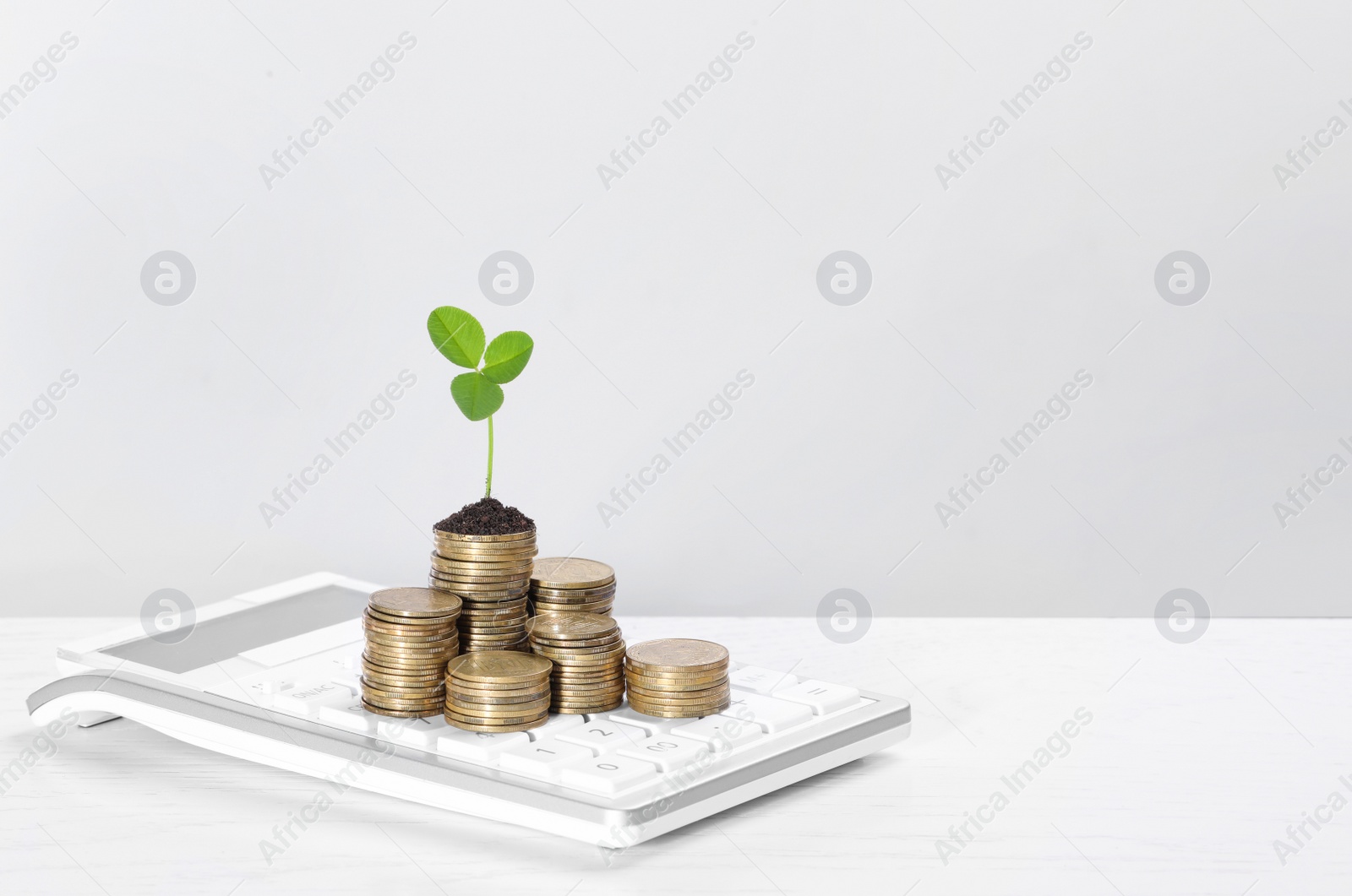 Photo of Stacks of coins with green sprout and calculator on white table, space for text. Investment concept