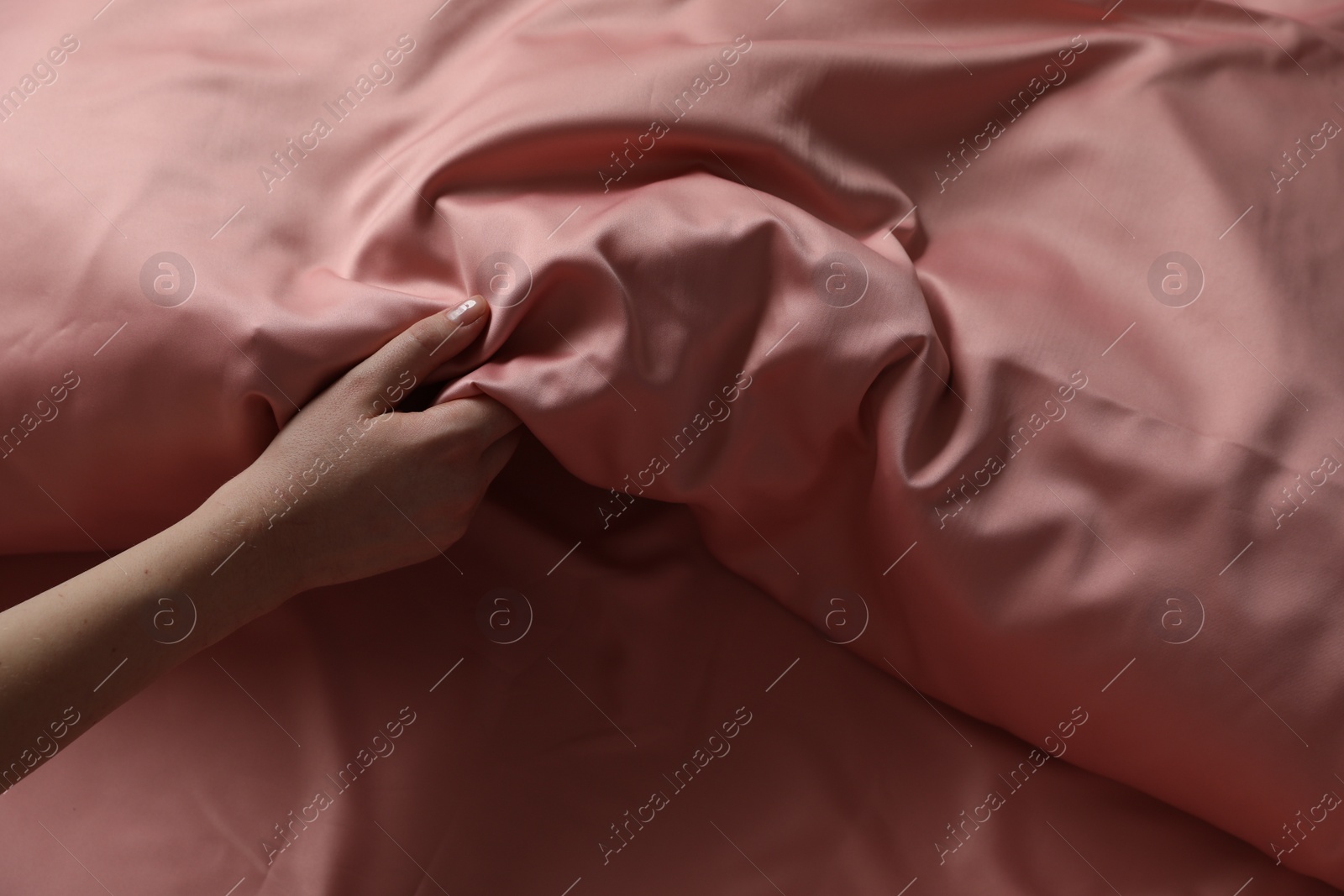 Photo of Woman making bed with beautiful pink silk linens, closeup view