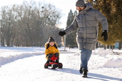 Photo of Family time. Father pulling his happy son on sledge in snowy park. Space for text