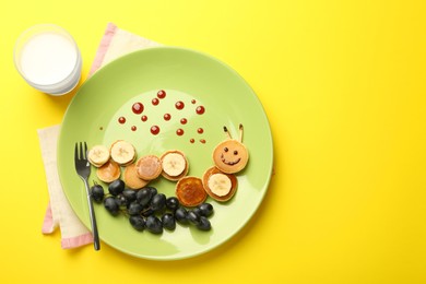 Photo of Creative serving for kids. Plate with cute caterpillar made of pancakes, grapes and banana on yellow background, flat lay. Space for text