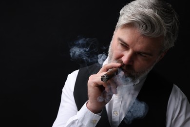 Photo of Bearded man smoking cigar against black background. Space for text