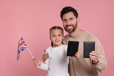 Immigration. Happy man with his daughter holding passports and flag of United Kingdom on pink background
