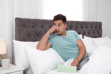 Photo of Young man suffering from allergy in bedroom