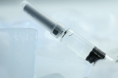 Photo of Syringe with COVID-19 vaccine on ice cubes, closeup