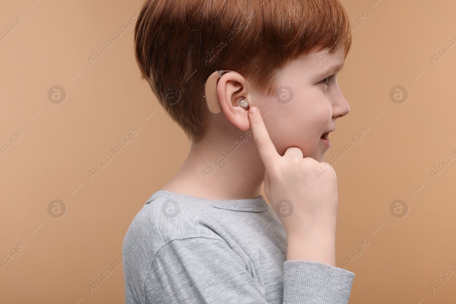 Photo of Little boy with hearing aid on pale brown background, closeup