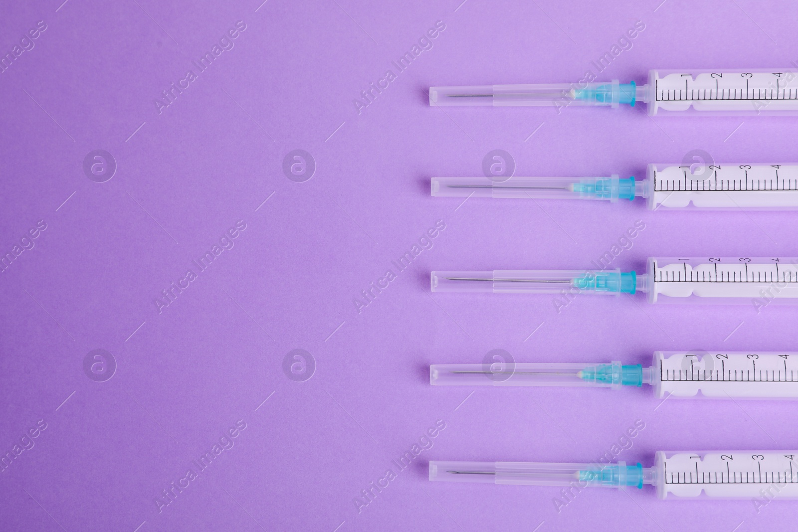 Photo of Disposable syringes with needles on violet background, flat lay. Space for text