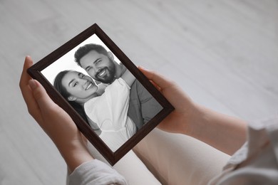 Woman holding frame with black and white photo portrait of young couple indoors, closeup