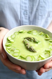 Photo of Woman holding bowl with delicious asparagus soup, closeup