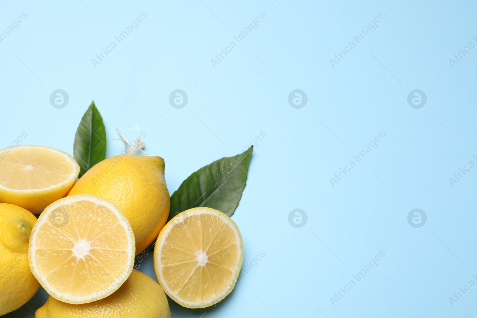 Photo of Many fresh ripe lemons with green leaves and flower on light blue background, flat lay. Space for text