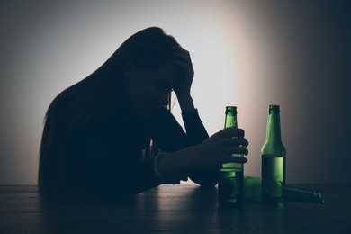 Photo of Alcohol addiction. Silhouette of woman holding beer bottle at table, backlit