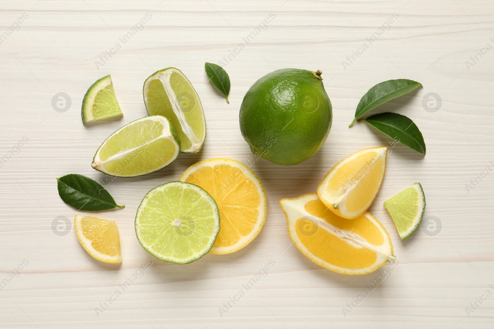 Photo of Fresh ripe lemons, limes and green leaves on white wooden background, flat lay