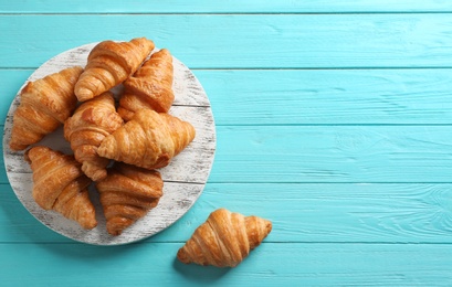 Photo of Board with tasty croissants and space for text on light blue background, flat lay. French pastry