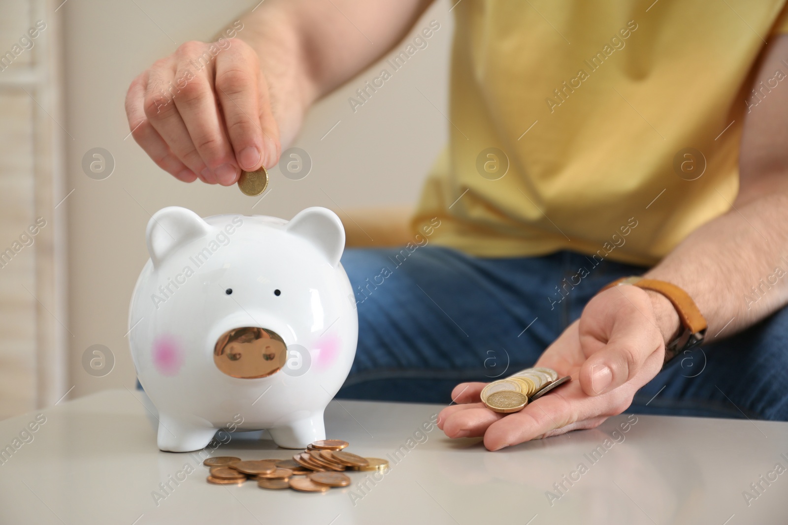 Photo of Man putting coin into piggy bank at table indoors, closeup. Money saving