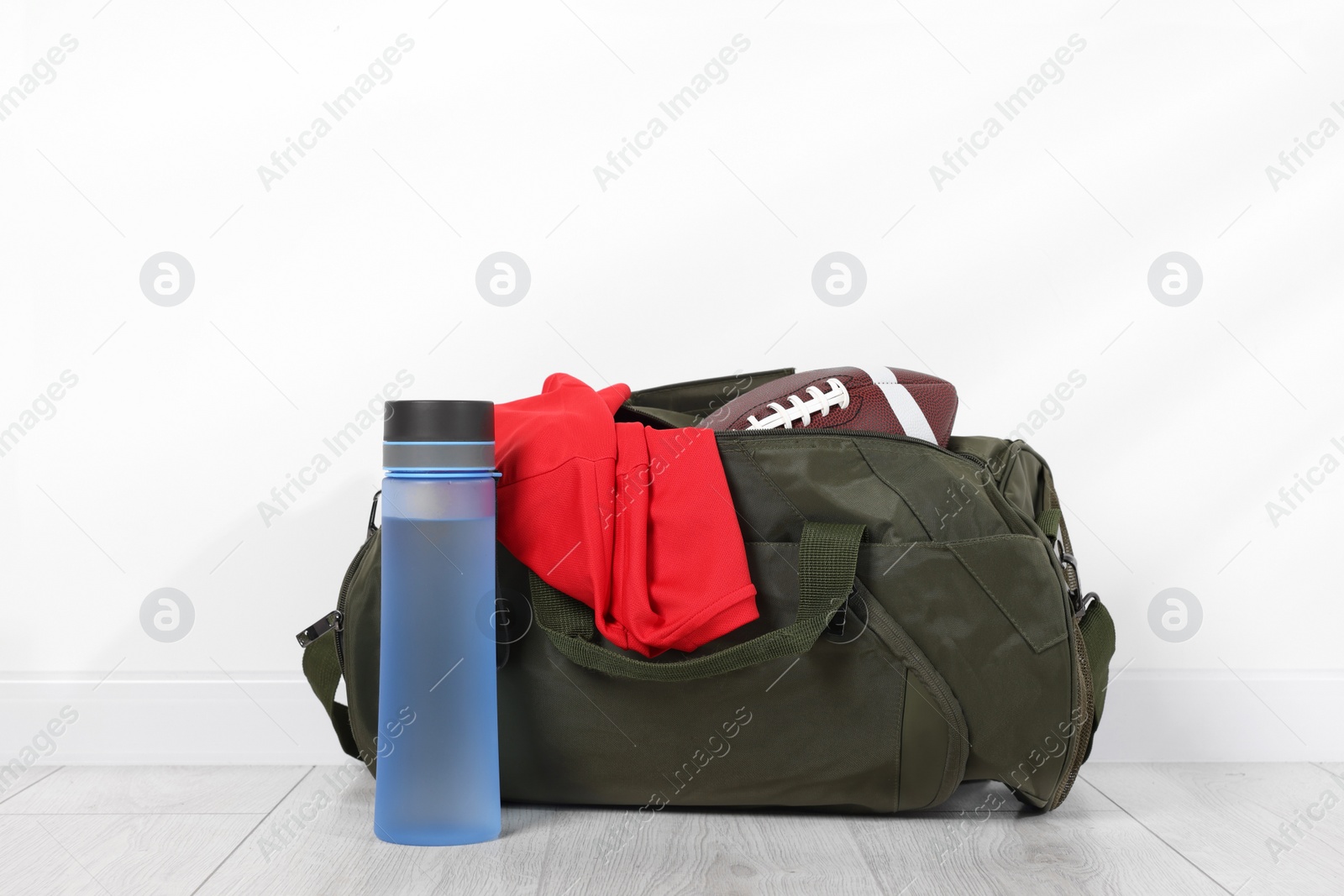 Photo of Gym bag and sports equipment on floor near white wall