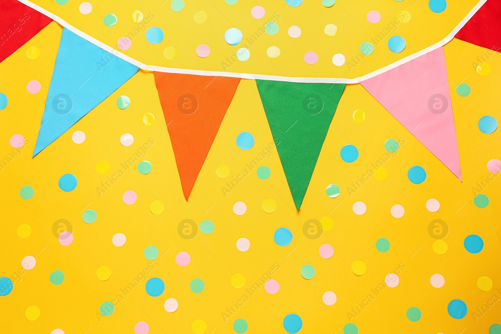 Photo of Bunting with colorful triangular flags and confetti on yellow background, flat lay