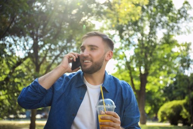 Young man with refreshing drink talking on smartphone in park