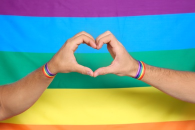 Photo of Gay couple making heart shape with their hands against rainbow flag, closeup