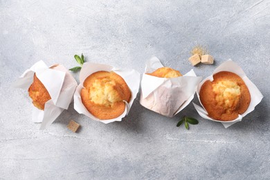 Photo of Delicious sweet muffins and brown sugar on light grey textured table, flat lay