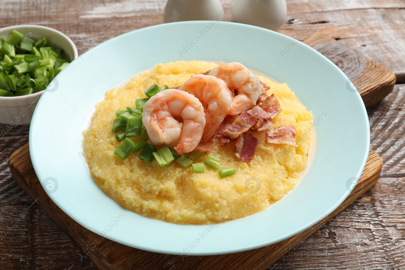 Photo of Plate with fresh tasty shrimps, bacon, grits and green onion on wooden table