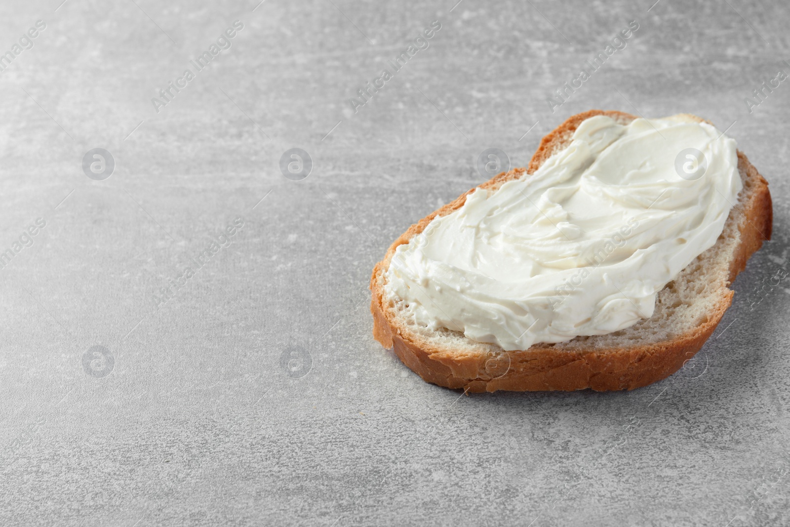 Photo of Slice of bread with tasty cream cheese on light grey table, space for text