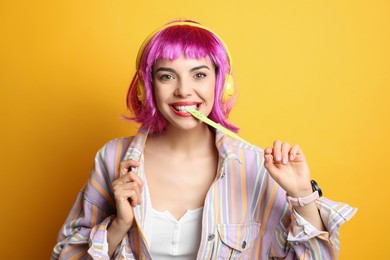 Photo of Fashionable young woman in colorful wig with headphones chewing bubblegum on yellow background