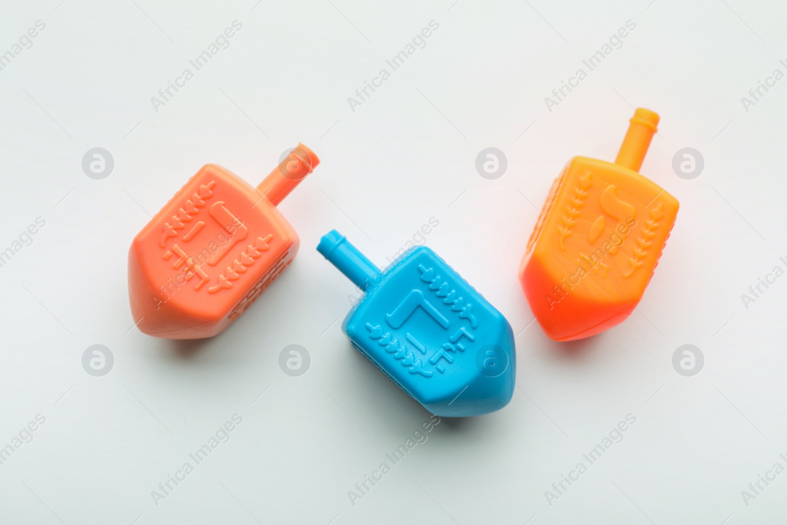 Photo of Colorful dreidels on white background, flat lay. Traditional Hanukkah game