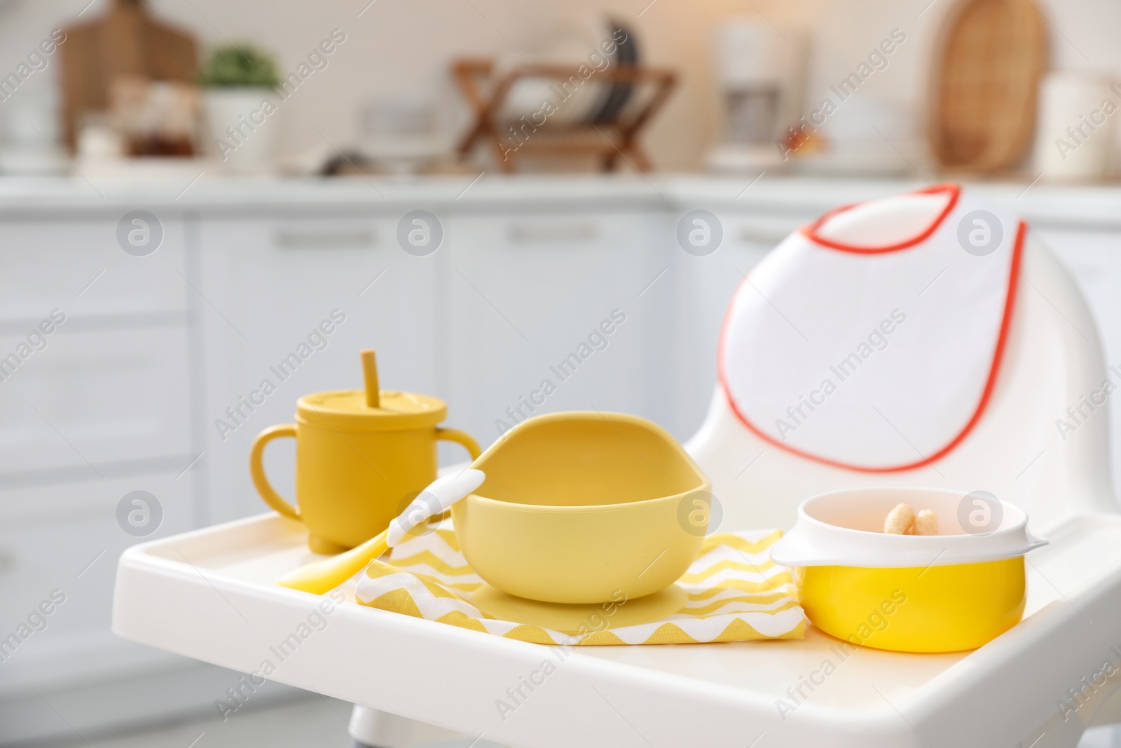 Photo of High chair with set of baby tableware on tray indoors