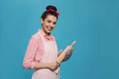 Photo of Young housewife in oven glove holding roller pin on light blue background, space for text