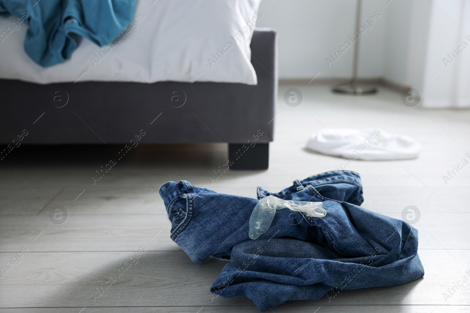 Photo of Unrolled condom and jeans on floor in bedroom. Safe sex