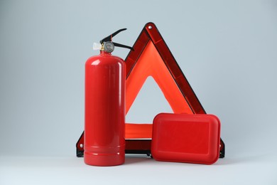 Emergency warning triangle, red fire extinguisher and first aid kit on light grey background. Car safety