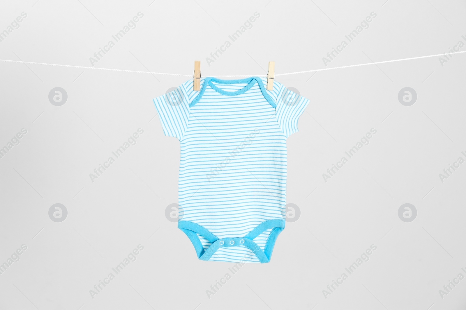 Photo of Cute baby onesie hanging on clothes line against light grey background. Laundry day