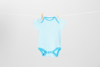 Photo of Cute baby onesie hanging on clothes line against light grey background. Laundry day