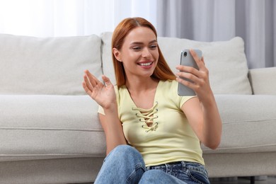 Happy young woman having video chat via smartphone at home