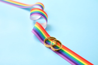 Wedding rings and rainbow ribbon on color background. Gay symbol