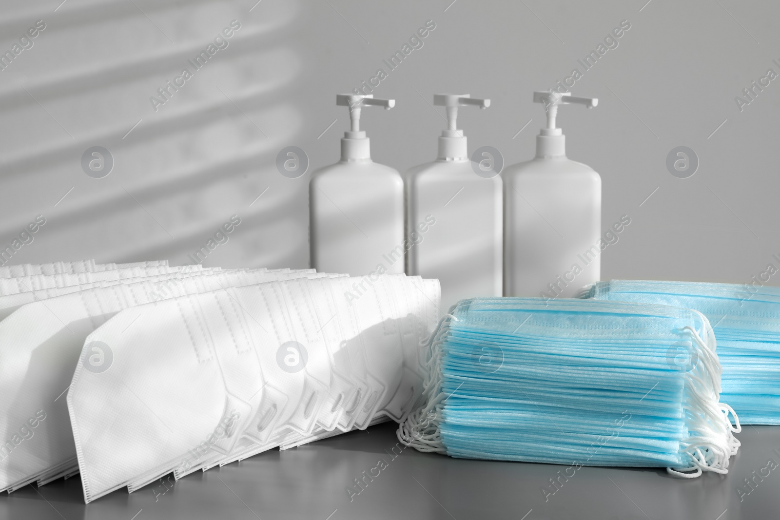 Photo of Hand sanitizers and respiratory masks on grey table indoors. Protective essentials during COVID-19 pandemic