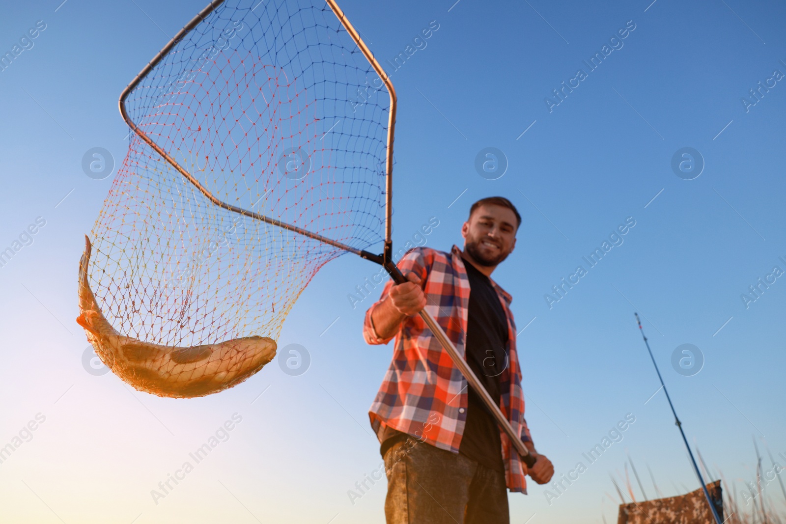 Photo of Fisherman holding fishing net with catch against blue sky, low angle view