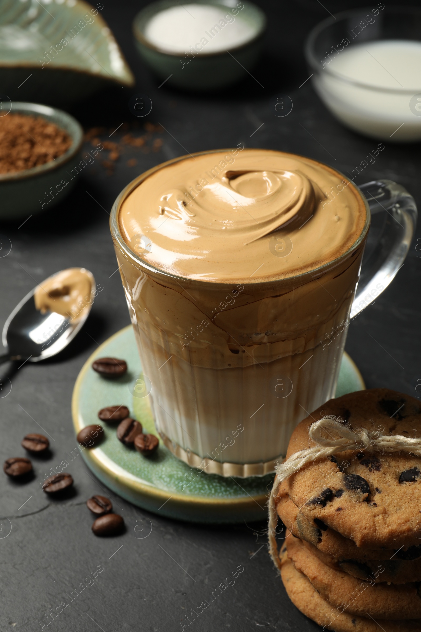 Photo of Glass mug of delicious dalgona coffee and chocolate chip cookies on dark table